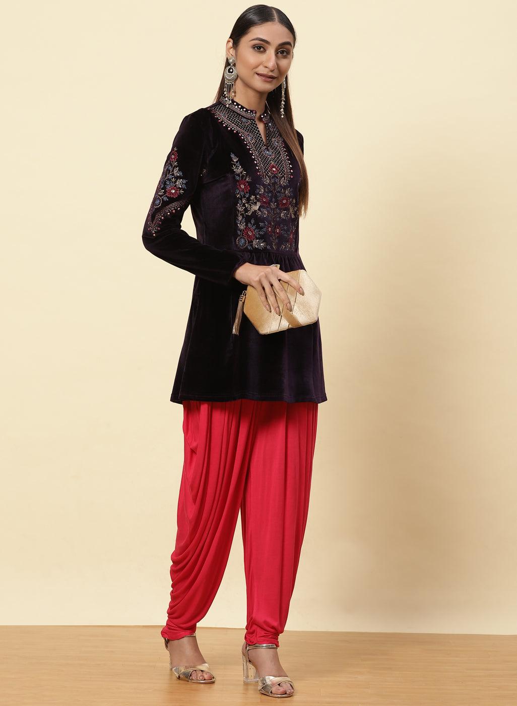 The woman is posing with Velvet Flared Tunic from Lakshita, red patiala, and a clutch 