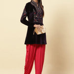 The woman is posing with Velvet Flared Tunic from Lakshita, red patiala, and a clutch 