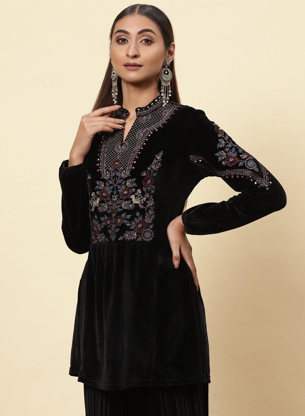 The woman is giving a stylish pose, wearing a black velvet kurti with beautifully decorated floral motifs