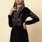 The woman is giving a stylish pose, wearing a black velvet kurti with beautifully decorated floral motifs