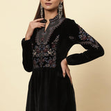 The woman is giving a stylish pose, wearing a black velvet kurti with beautifully decorated floral motifs