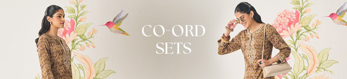 A woman in Lakshita pastel blue co-ord set with floral cutwork, walking through a lush garden under soft sunlight