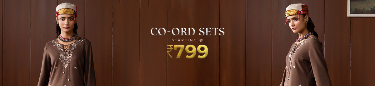 A woman in Lakshita pastel blue co-ord set with floral cutwork, walking through a lush garden under soft sunlight