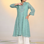 Woman smiling in Fariha Carnation Green Embroidered Raschel Net Dress paired with white palazzos and golden pumps