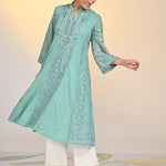 Woman swaying in Fariha Carnation Green Embroidered Raschel Net Dress paired with white palazzos and golden pumps