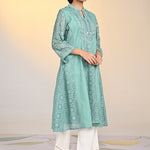 Woman walking wearing Fariha Carnation Green Embroidered Raschel Net Dress paired with white palazzos and golden pumps